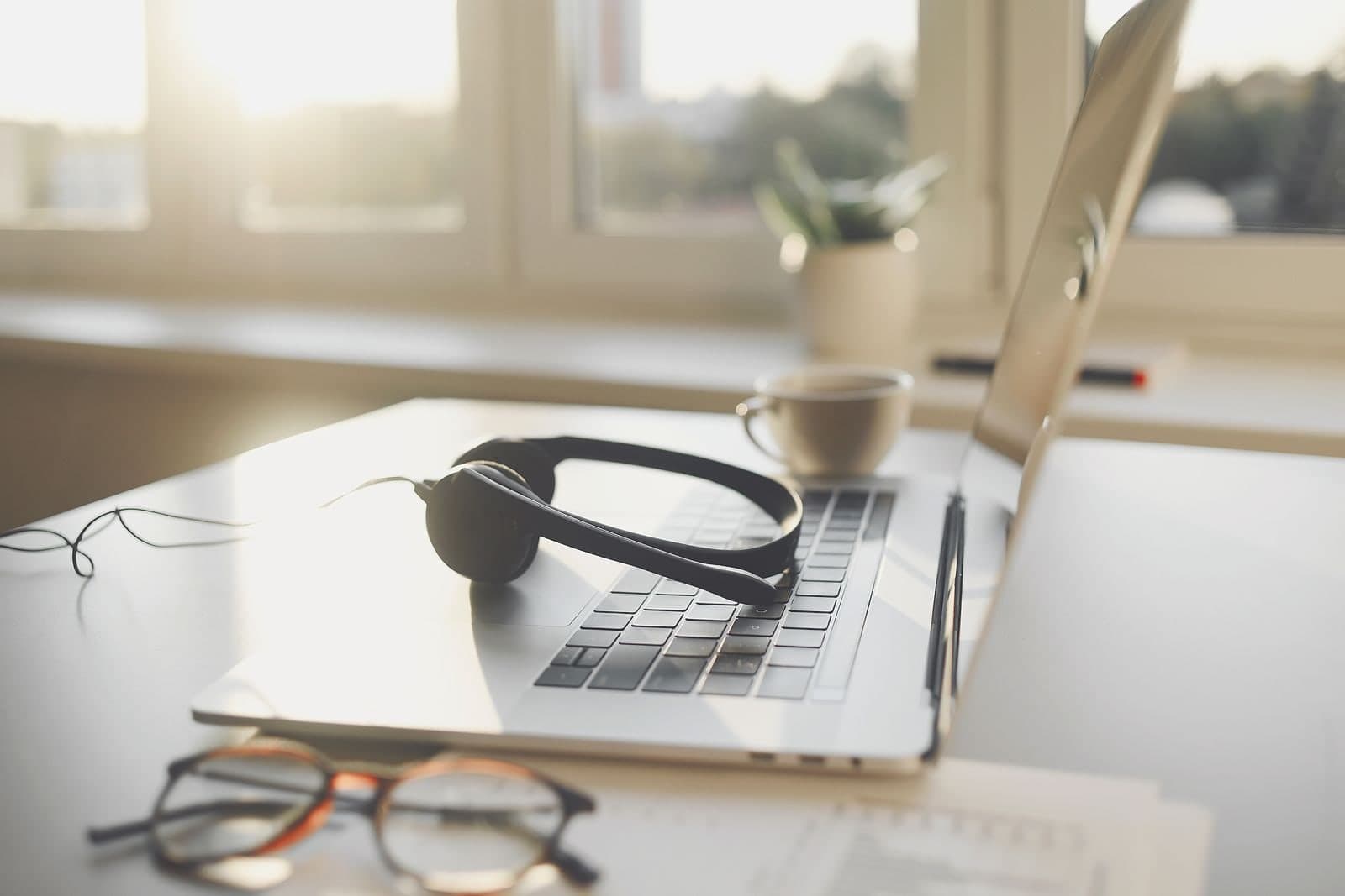 A phone headset resting on an open laptop, with reading glasses on the desk beside it.