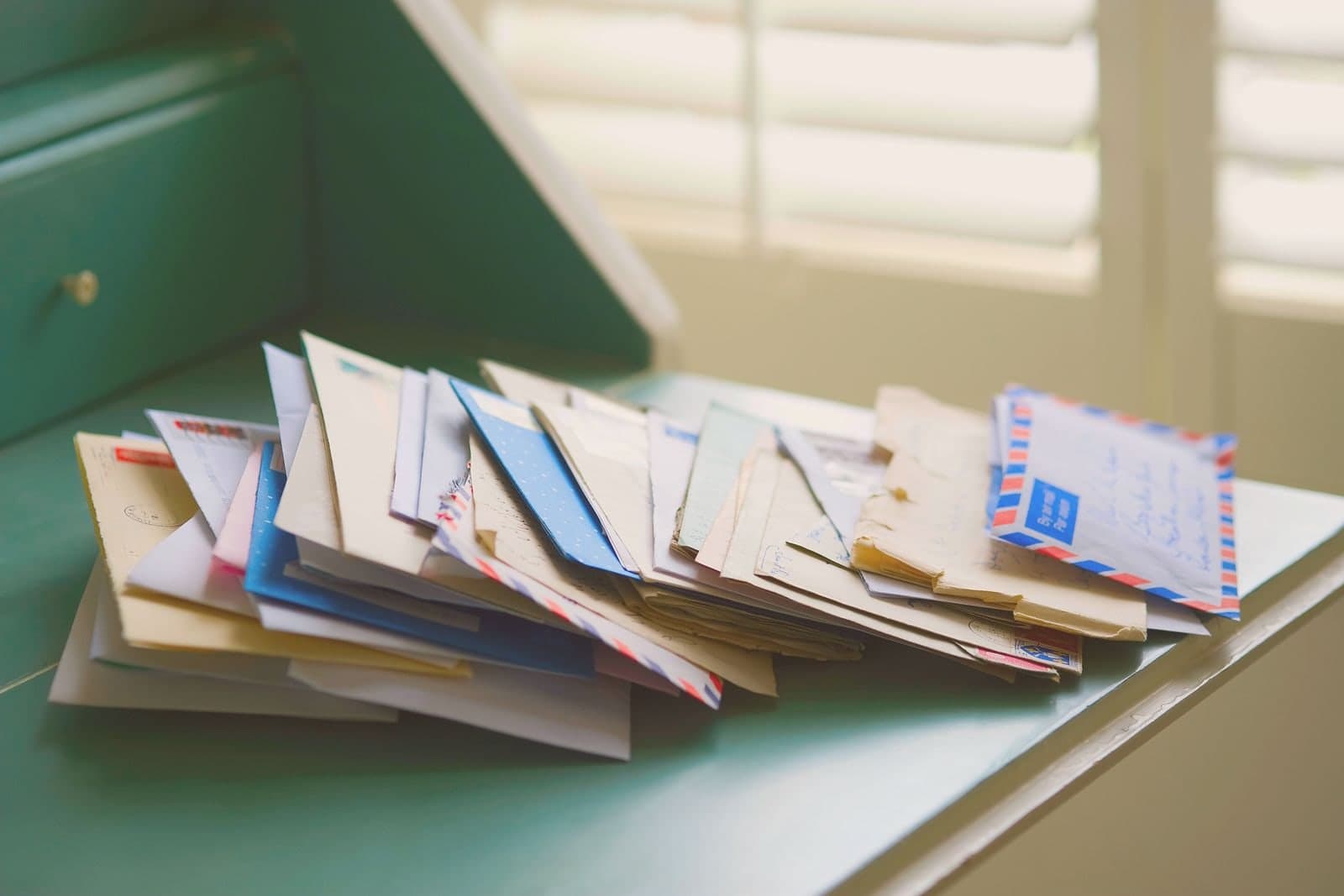 A heap of unopened mail spilling across a table by a window.
