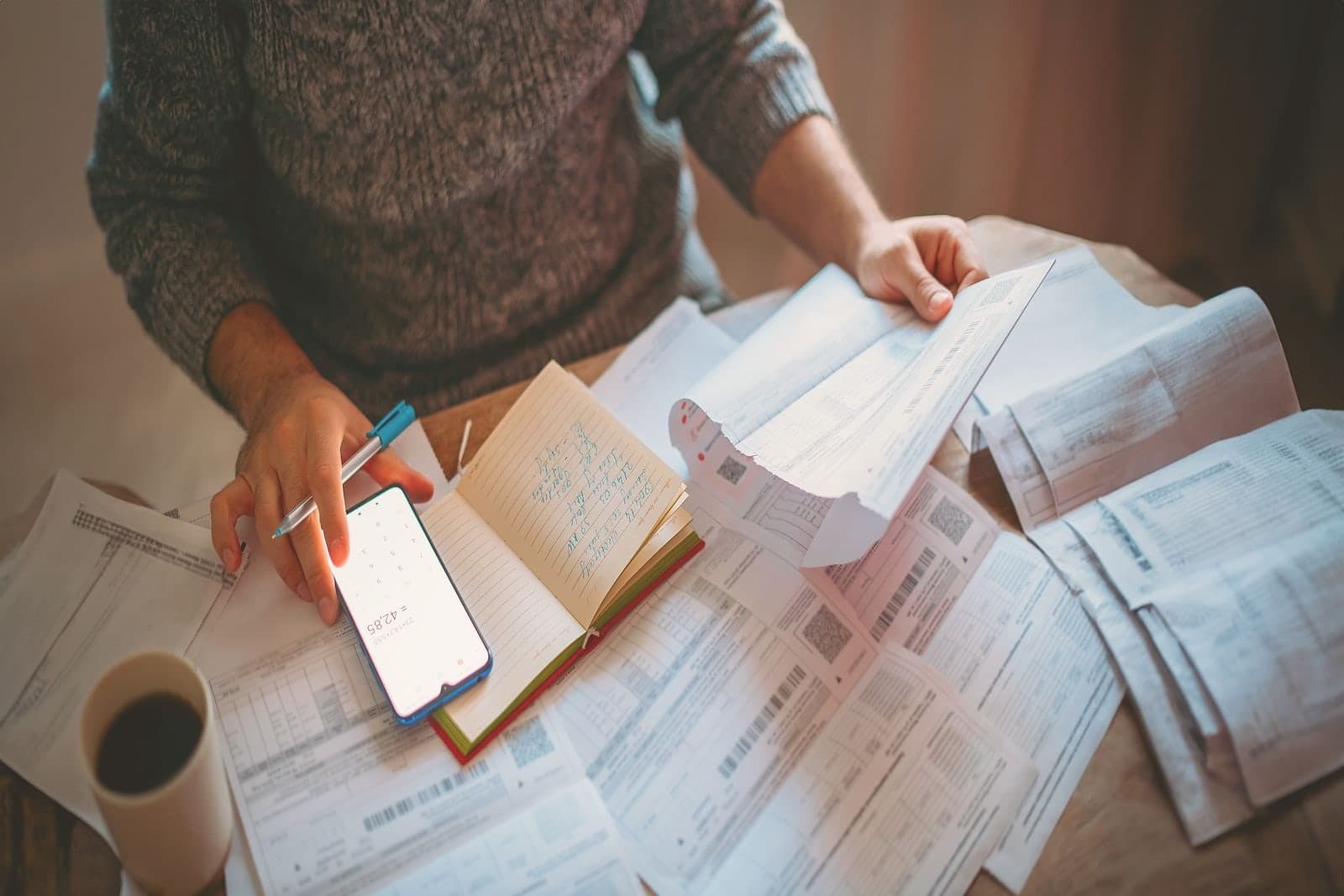 Someone at a table with a pen, a notebook and a spread of statements.