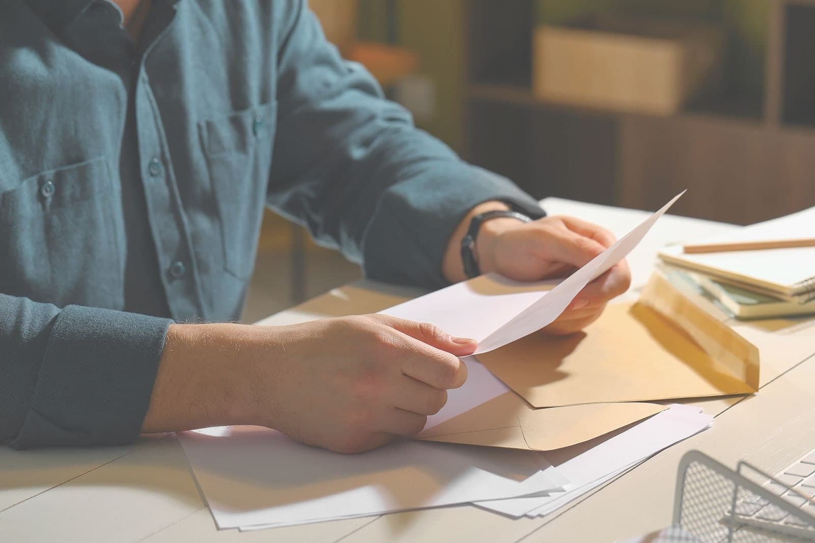 Hands drawing a letter out of a large brown envelope at a kitchen table.