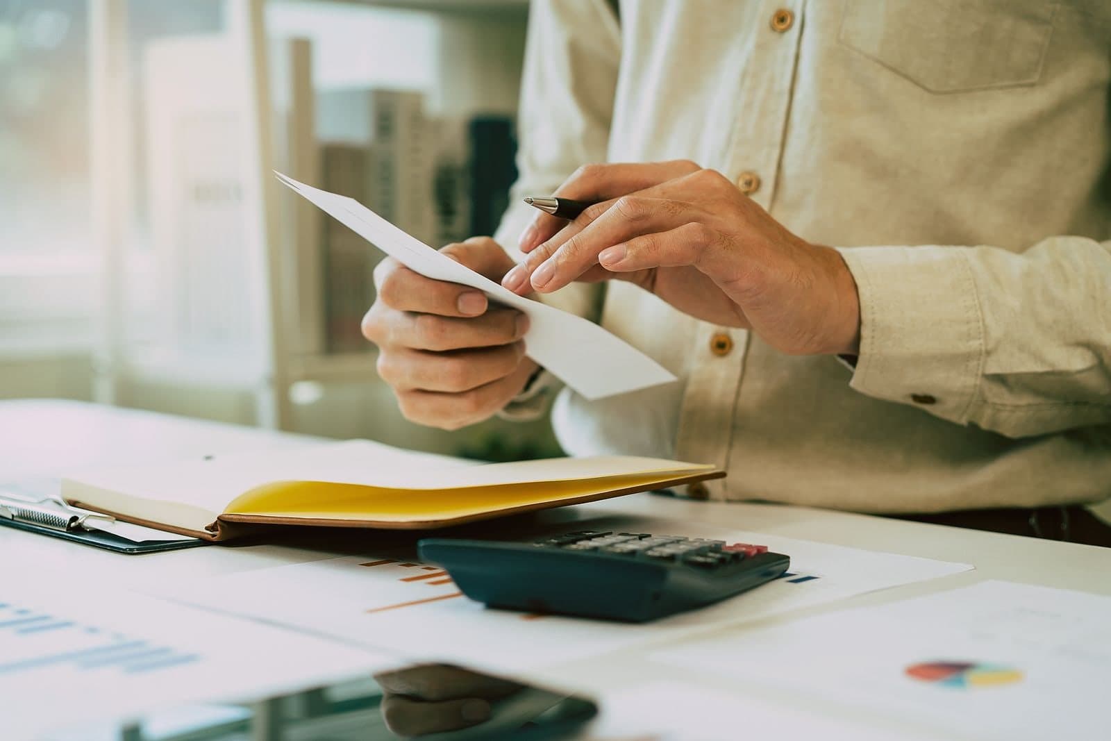 Someone at a desk holding a single sheet of paper, pen in the other hand.