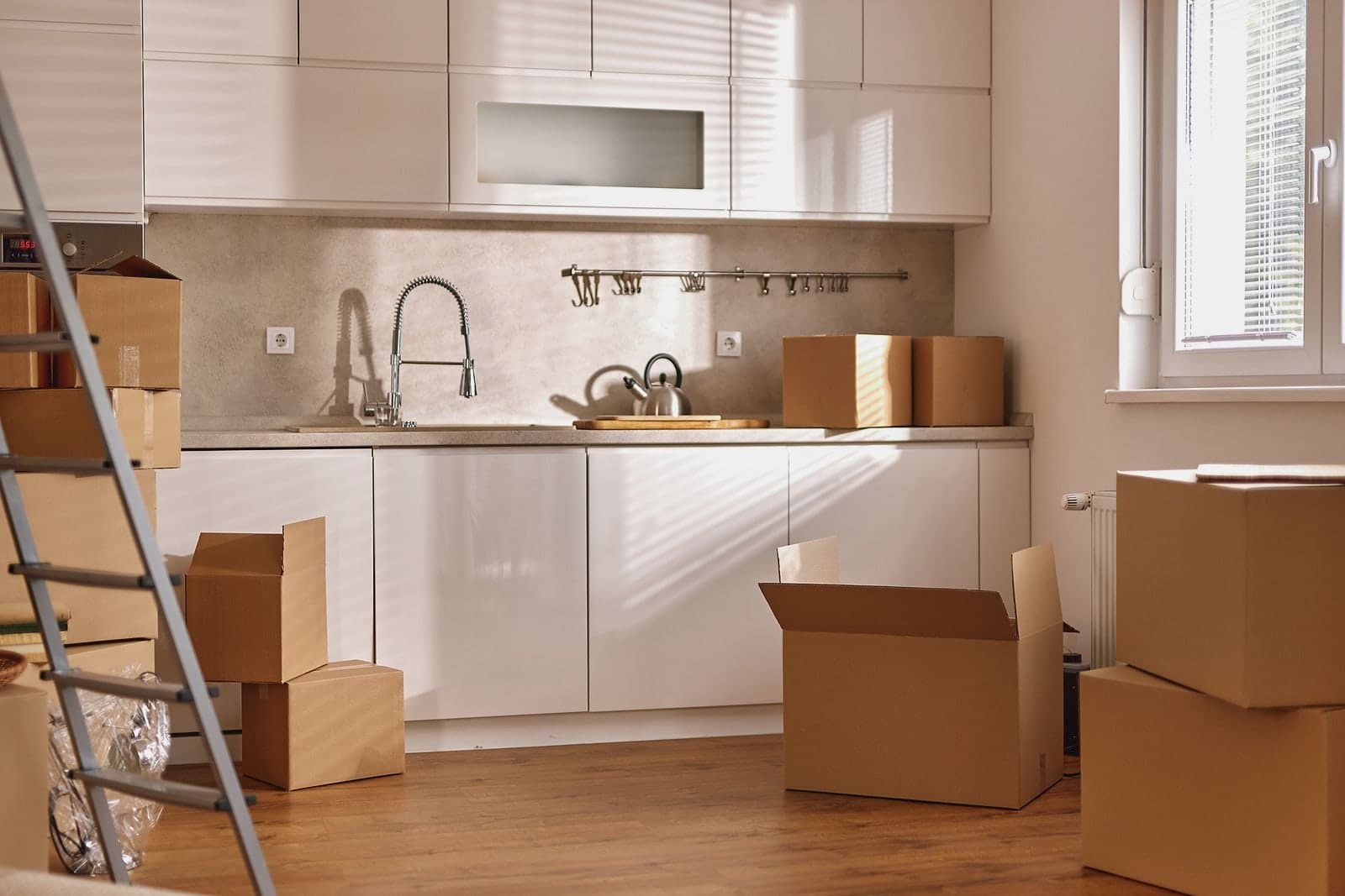 Moving boxes stacked across an empty kitchen floor, a ladder against the wall.