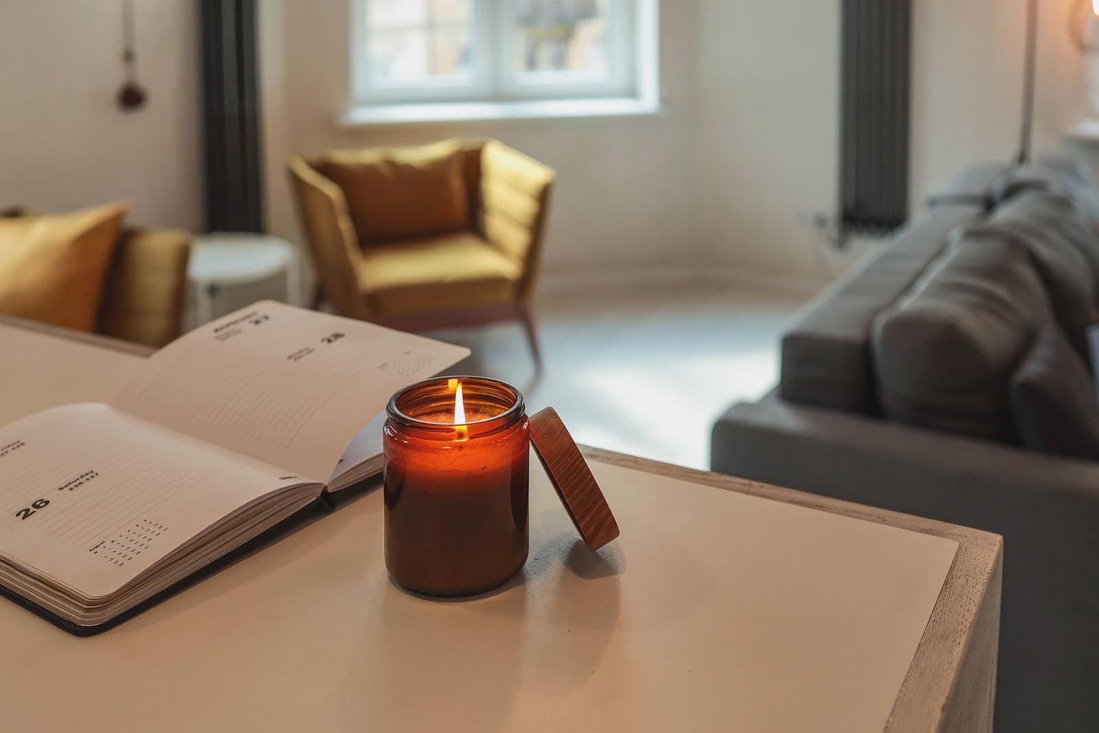 A planner lying open on a table beside a lit candle, armchairs and a window behind.