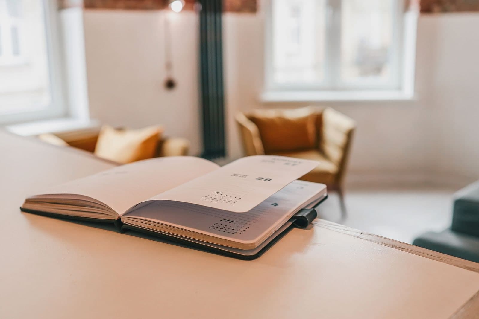 A dated planner open on a table in a bright room, an armchair by the window behind it.