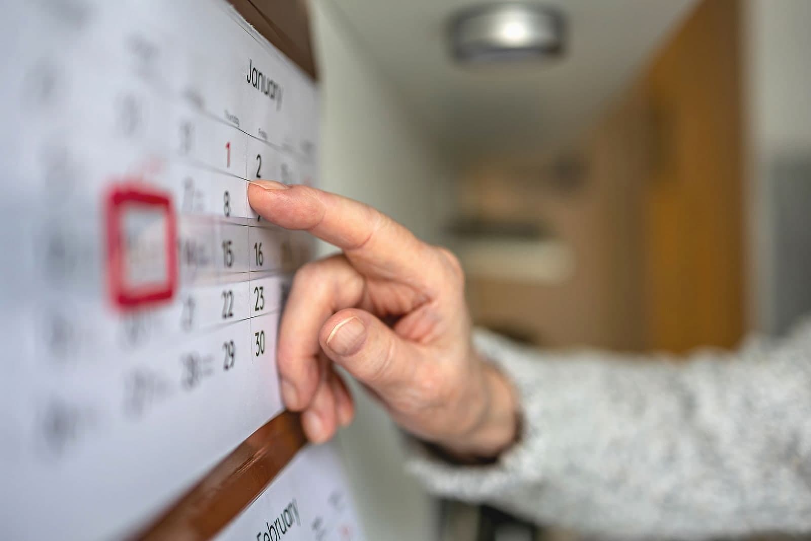 A hand at a wall calendar, one date ringed in red.